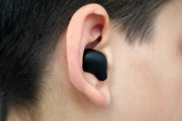 un niño con un auricular bluetooth en el oído escucha música, - Foto, imagen