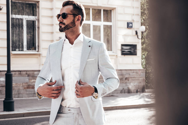 Portrait of handsome confident stylish hipster lambersexual model.Modern man dressed in elegant white suit. Fashion male posing in the street background in Europe city at sunset. In sunglasses - Photo, Image
