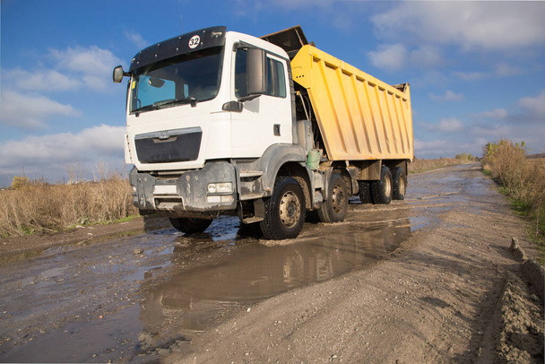 dump truck met een geel lichaam rijdt op een onverharde weg na regen tegen een blauwe lucht. Het proces van transport en lossen van de bodem op bouwmachines. Bedrijfsvoertuigen - Foto, afbeelding