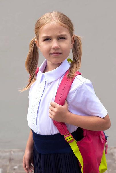 Egy gyönyörű kis iskoláslány rózsaszín hátizsákkal sétál a parkban, az iskolába való visszatérés koncepciója. Iskola egyenruha. - Fotó, kép