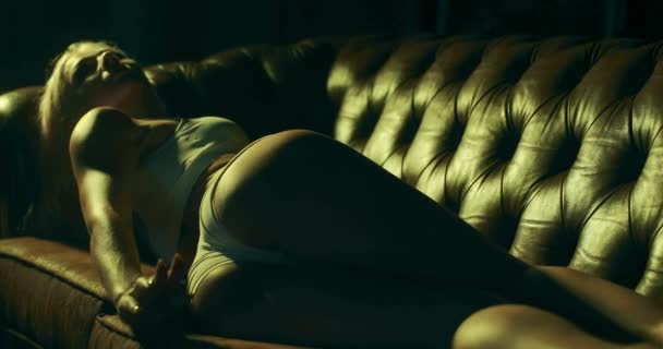 Jovem mulher encantadora sedutoramente deitada em um sofá em uma sala de estar escura. - Filmagem, Vídeo