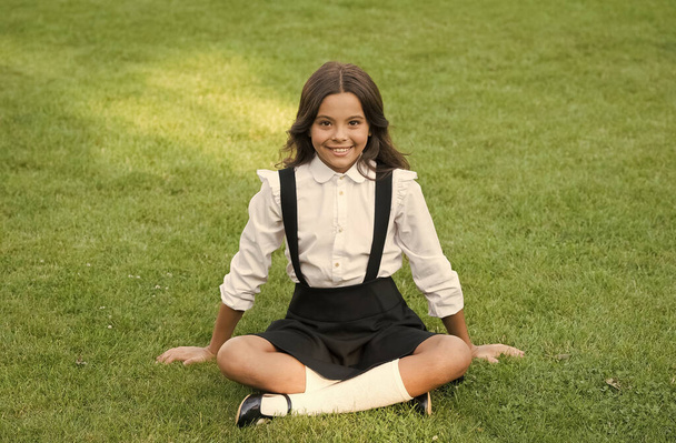 Pride In Excellence. cute smiling confident schoolgirl relax on green grass. happy childhood. back to school. Small girl wear school uniform. beauty and fashion. beautiful student teen girl in park - Fotografie, Obrázek