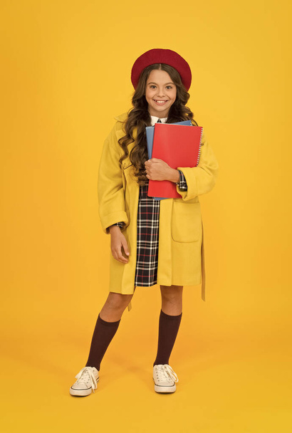 nice smile. little girl with notebook or workbook for lesson. education concept. school and fashion. child in pupil uniform. kid in french beret on yellow background. stylish teen college student - Photo, image
