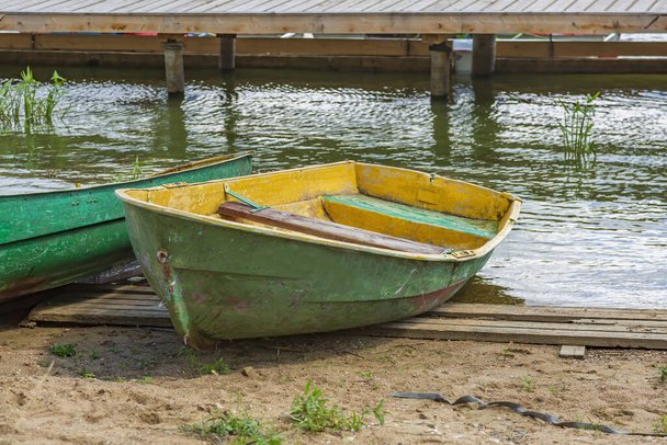 池の岸に川の散歩のための空のみすぼらしいプラスチック製のボートが立っている - 写真・画像