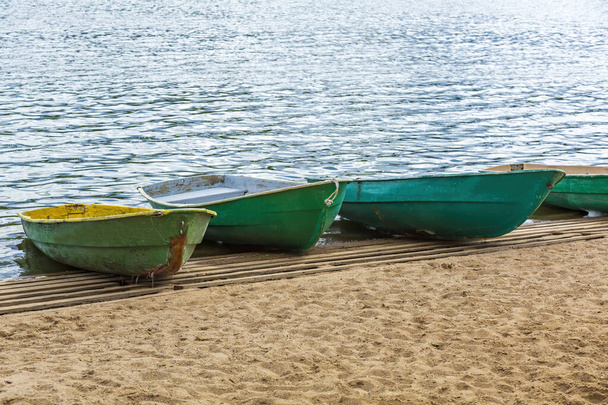 池の岸に川の散歩のための空のみすぼらしいプラスチック製のボートが立っている - 写真・画像