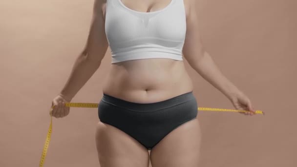 Donna sovrappeso in biancheria intima misurare il suo ventre grasso con nastro di misura. Studio ancora girato video. - Filmati, video
