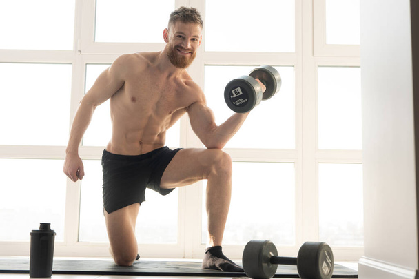 Sportsman do exercise with dumbbell on fitness mat - Photo, Image