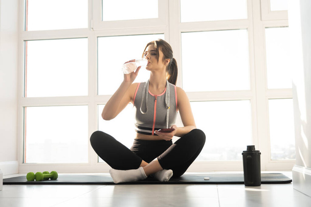 Woman drinking water from bottle on fitness mat - Foto, Bild