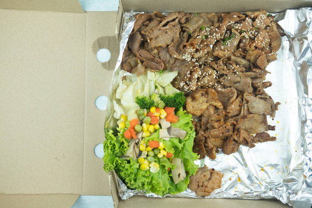 Koreaans gegrild varkensvlees met groente geserveerd in folie papier op doos. - Foto, afbeelding