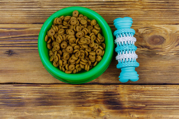Dog toy and dry dog food in green plastic bowl on wooden background. Top view. Dog care concept - Photo, Image
