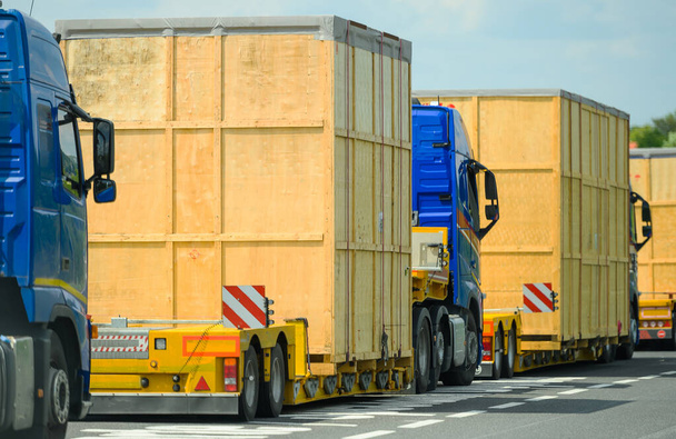Heavy Oversize Load Convoy en la ruta hacia el destino. Pocos camiones semi tirando grandes contenedores de madera de gran tamaño. Industria del transporte. - Foto, Imagen