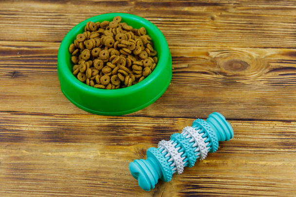 Juguete para perros y comida seca para perros en un tazón de plástico verde sobre fondo de madera. Concepto de cuidado del perro - Foto, imagen