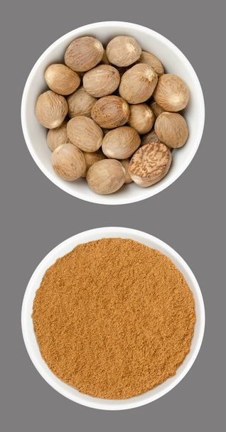 Whole nutmegs and nutmeg powder, in white bowls, on gray background. Fragrant or true nutmeg, dried seeds of Myristica fragrans, a spice, also used in traditional medicine. Close-up from above, photo. - Photo, Image