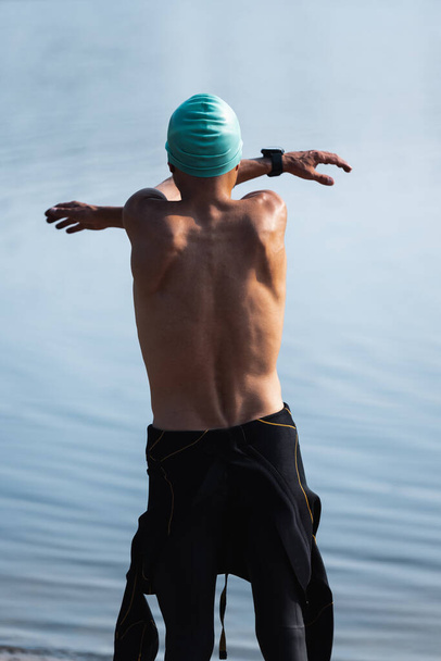 Profi triatlonista úszás előtt a folyókban nyílt víz. A férfi úszó felszerelést visel, triatlont gyakorol a strandon nyáron.. - Fotó, kép