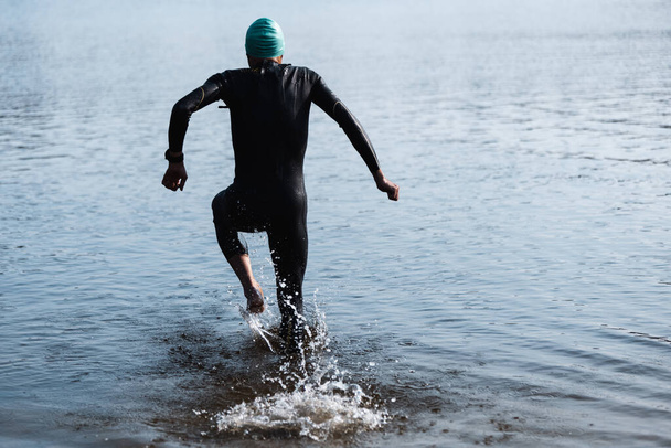 Profi triatlonista úszás folyókban nyílt vízben. A férfi úszó felszerelést visel, triatlont gyakorol a strandon nyáron.. - Fotó, kép