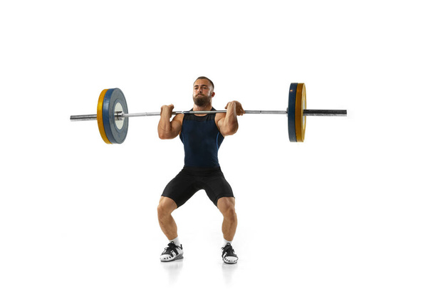 Ganzkörperporträt eines Mannes in Sportbekleidung, der mit einem Gewicht trainiert, das auf weißem Hintergrund isoliert ist - Foto, Bild
