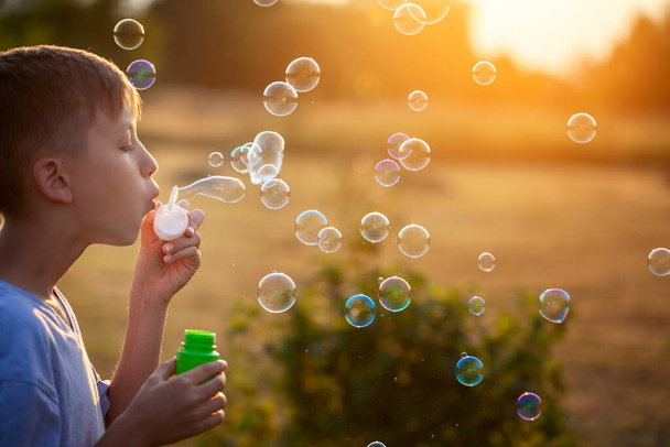 Child blowing soap bubbles on a summer day at sunset nature. Concept happy childhood. - Foto, afbeelding