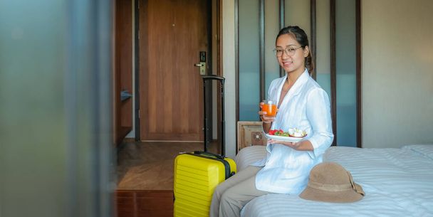 Foto de una mujer de negocios comiendo frutas y bebiendo jugo de naranja en la cama en la habitación de hotel de lujo, concepto de comida saludable. - Foto, imagen