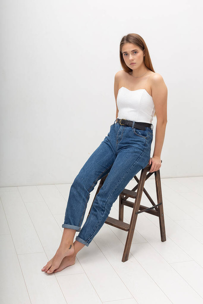 young caucasian woman with long brown hair in in corset, blue jeans at studio - Photo, image