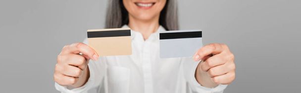 vue recadrée d'une femme souriante floue montrant des cartes de crédit isolées sur gris, bannière - Photo, image