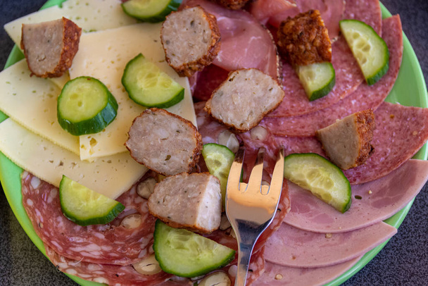 Heerlijke koude lunch met diverse vleeswaren waaronder pittige salami en gehaktbrood geserveerd met kaas en verse komkommer in een close-up top down uitzicht met vork - Foto, afbeelding