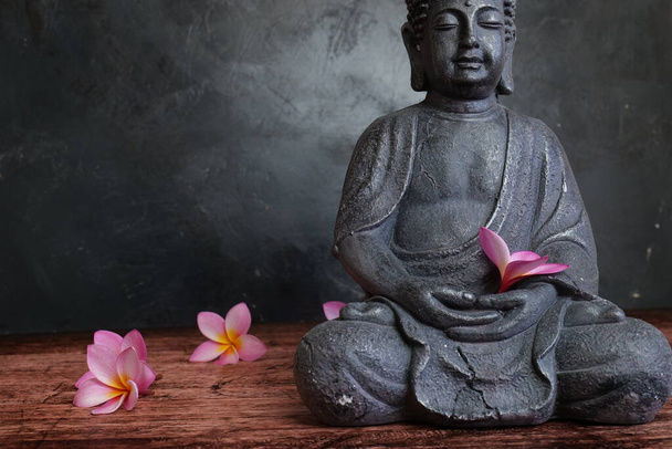 Статуя Будди з квітами франгіпані на темному тлі
 - Фото, зображення
