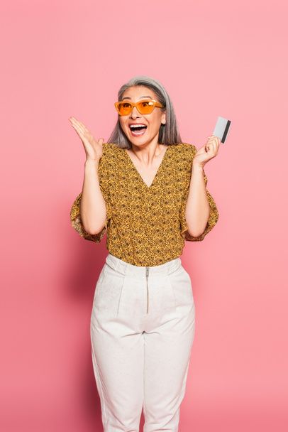 overjoyed asian woman with credit card showing wow gesture on pink background - Foto, Imagem