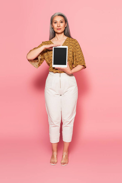 full length view of asian woman in stylish clothes holding digital tablet with blank screen on pink - Фото, изображение