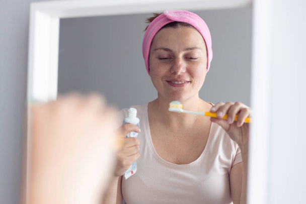 Femme brossant les dents serrant le dentifrice à la menthe sur une brosse à dents en plastique, prenant soin de la respiration fraîche et de la prévention des caries. - Photo, image