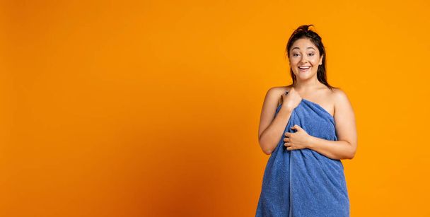 Urocza piękna pulchna kobieta z dużym ręcznikiem odizolowany nad pomarańczowym tle studio. - Zdjęcie, obraz