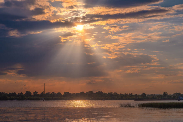Nehirde gün batımı. Güneş ışınları bulutların arasından yol alır. Hava güzel.. - Fotoğraf, Görsel