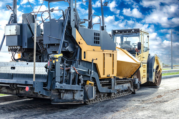 Asphalt paving equipment. Asphalt paver against the backdrop of a clear cloudy sky. Construction of new roads and road junctions. Heavy construction industrial machinery - Photo, Image