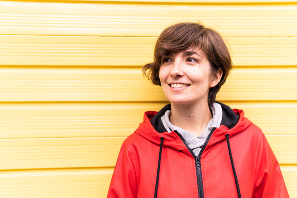 Foto di una giovane ragazza con un impermeabile rosso sorridente con uno sfondo giallo dietro di lei. - Foto, immagini