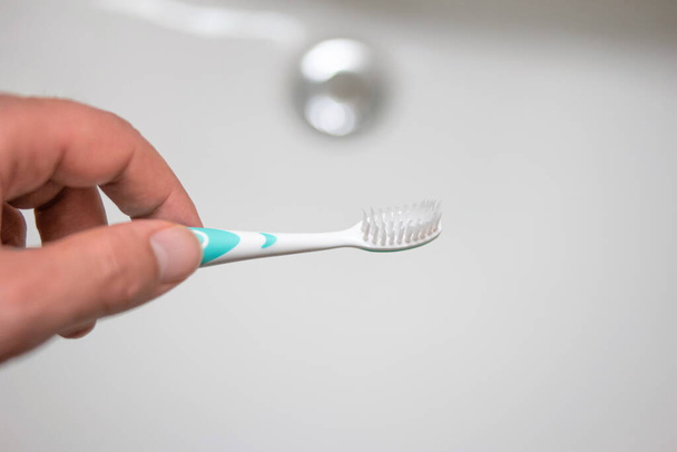Mão masculina segurando uma escova de dentes sobre pia do banheiro. - Foto, Imagem