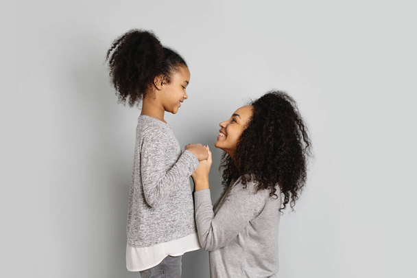 Mother and daughter looking each other in eyes on grey background. - Photo, image