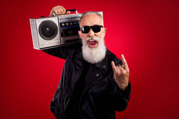 Photo of aged excited man happy positive smile hold boombox show rock sign brutal music lover isolated over red color background - Valokuva, kuva