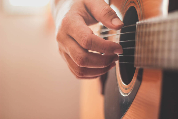 Κιθαρίστας παίζει κιθάρα σε ένα δωμάτιο με πλευρικό φωτισμό. - Φωτογραφία, εικόνα