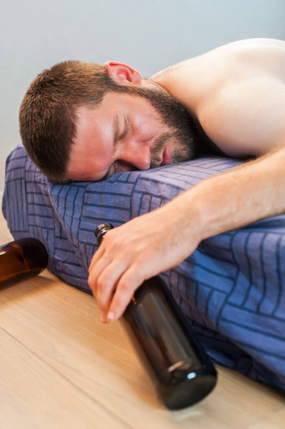 朝酔った男が酒を片手にベッドの上に横になっている。ハンガー症候群。アルコール依存症の概念  - 写真・画像