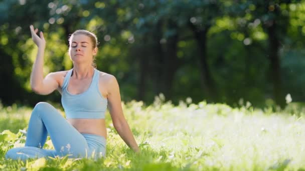 Młoda kobieta zmienia pozy relaksacyjne jogi na łące trawy - Materiał filmowy, wideo