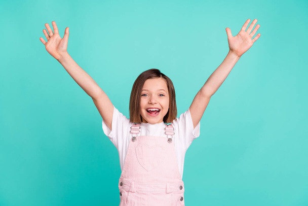 Photo of charming happy amazed little girl raise hands good mood winner isolated on teal color background - Foto, immagini