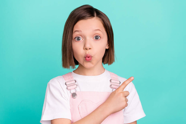 Photo of sweet excited school girl wear pink overall smiling pointing finger empty space isolated teal color background - Photo, image
