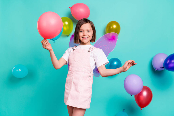 Photo of carefree sweet schoolgirl dressed pink overall wings holding colorful balloons isolated turquoise color background - Fotoğraf, Görsel