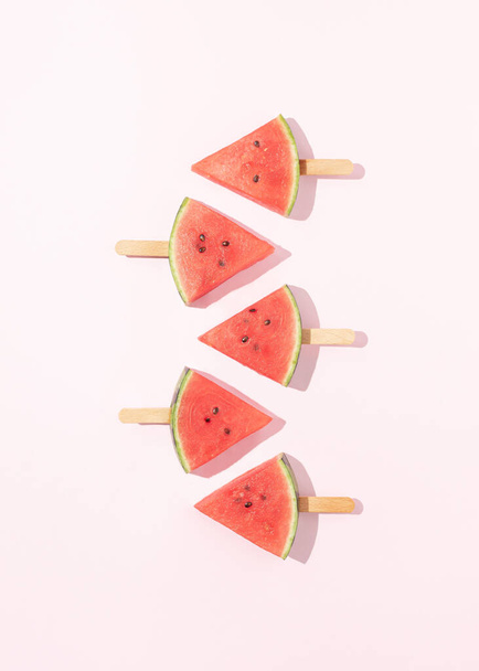 Paletas de sandía con sombra de luz solar sobre fondo rosa pastel. Concepto de frutas de fiesta de verano mínimo. Comida creativa. Puesta plana. - Foto, Imagen
