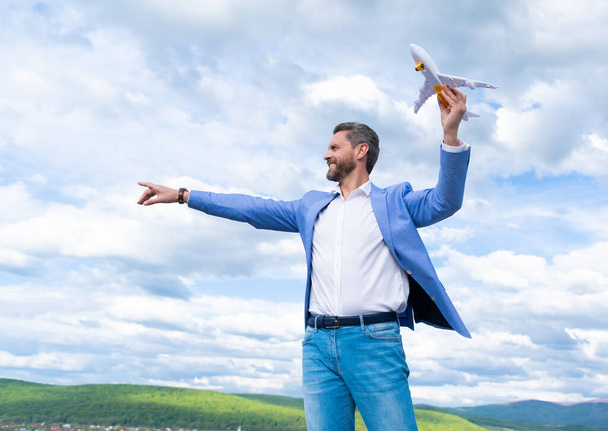 Dojrzałe szczęśliwy człowiek przedsiębiorca w kurtka trzymać zabawki samolot na tle nieba, wolność - Zdjęcie, obraz