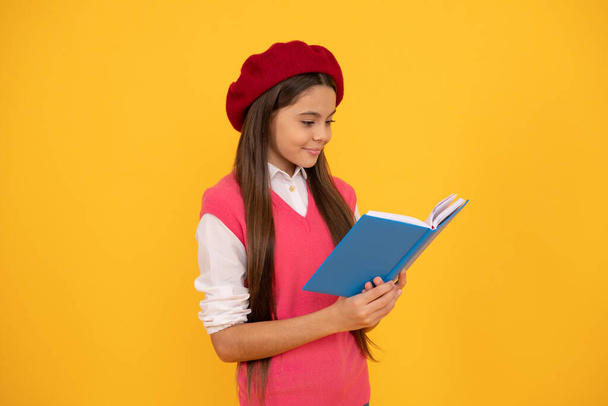 happy teen school girl in french beret reading book on yellow background, reading - Fotó, kép