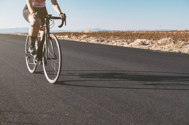 Close-up das pernas de uma ciclista feminina enquanto andava em uma estrada durante o pôr do sol. Conceito de ciclismo. Conceito de desporto. - Foto, Imagem