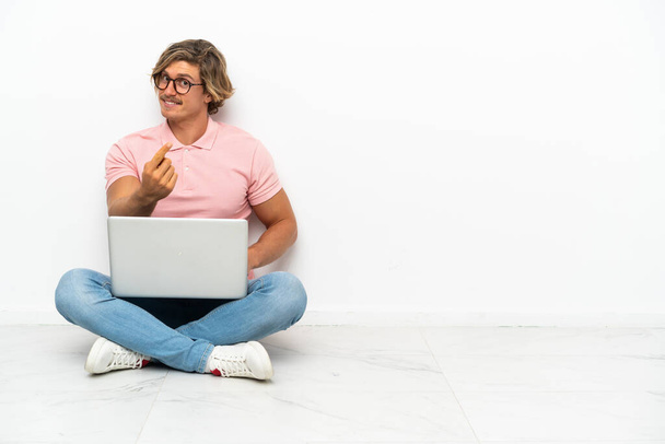 Young caucasian man sitting on the floor with his laptop isolated on white background doing coming gesture - Photo, image