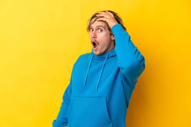 Handsome blonde man isolated on yellow background doing surprise gesture while looking to the side - Foto, Imagen