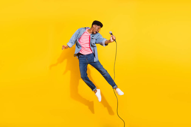 Full length photo of crazy dark skin happy man jump up hold microphone isolated on yellow color background - Φωτογραφία, εικόνα