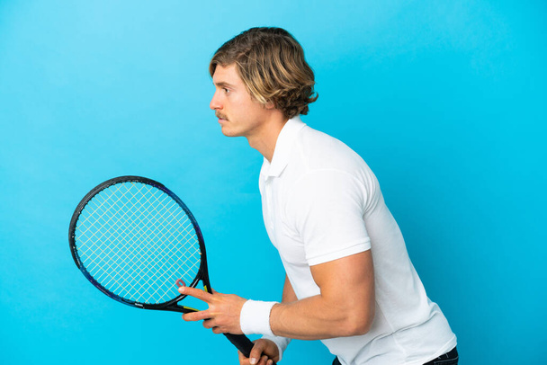 Giovane uomo biondo isolato su sfondo blu giocare a tennis - Foto, immagini